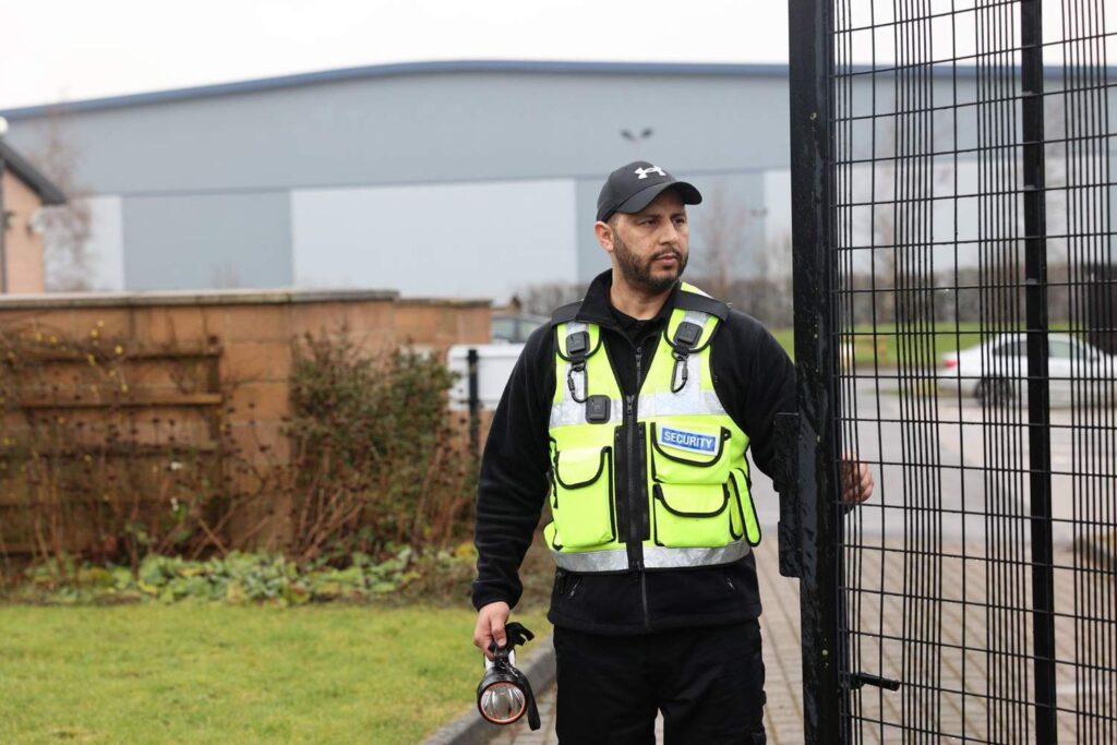 UK security officer wearing uniform patrolling a UK residential building and checking access points during daytime.