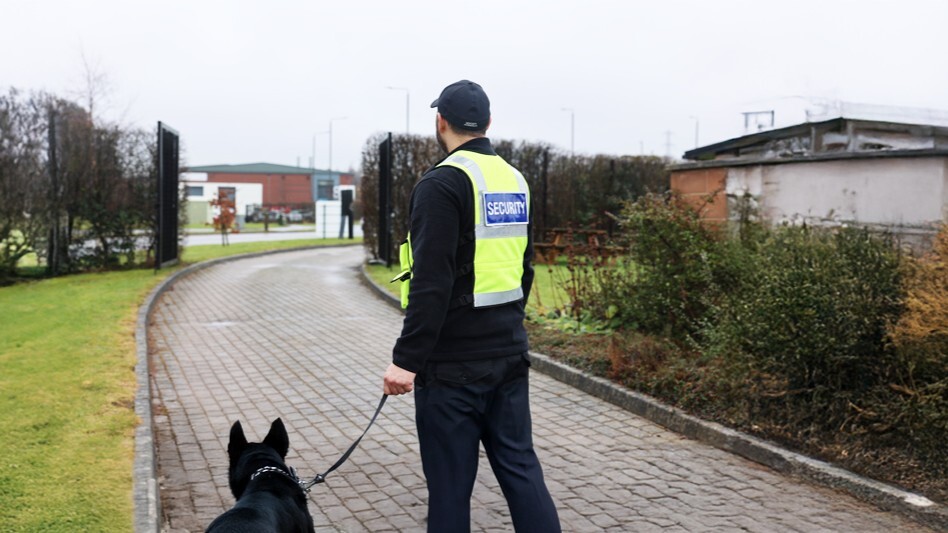 Security dog handler walking with a trained canine security dog around an industrial estate perimeter showing the importance of canine security.